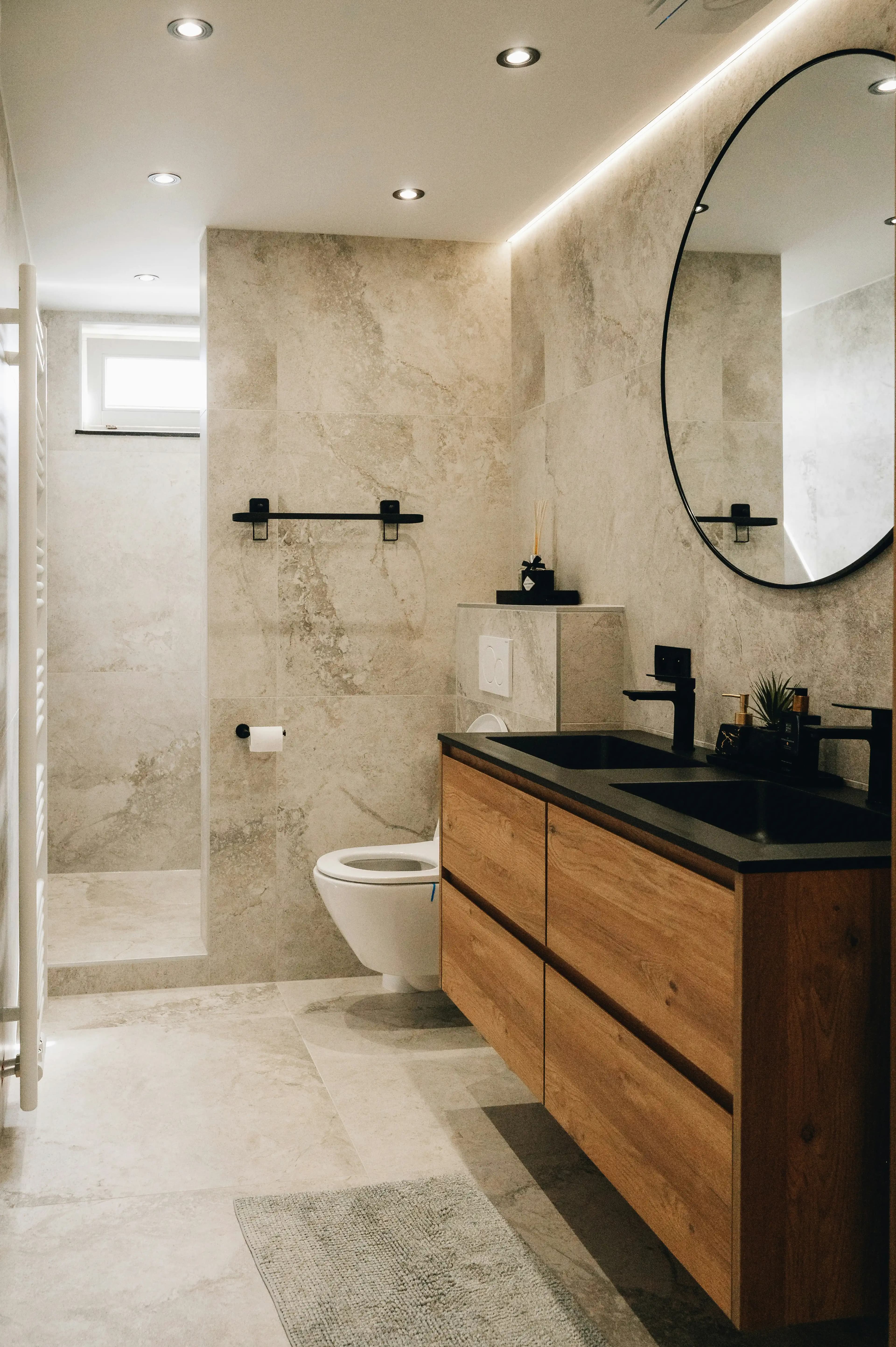 Clean bathroom with circular mirror on the wall, dark wooden sink cabinet and dark taps.